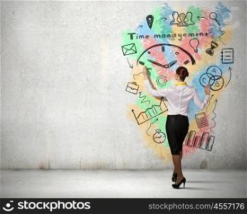 Manage your time effectively. Back view of businesswoman drawing time management concept on wall