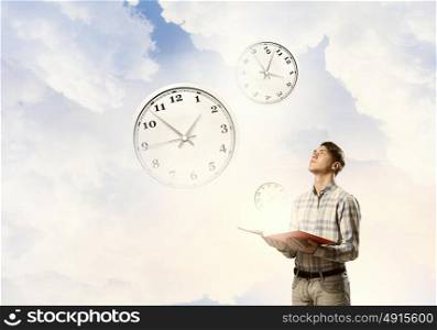 Manage your time. Young man with book in hands looking at clock