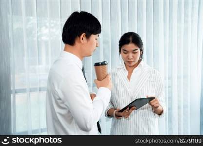 Manager advising guiding younger colleague with tablet in workplace. Couple businesspeople in formal wear working together on financial strategy as concept of teamwork and harmony in office.. Office colleague discussing business strategy for concept of harmony in office.