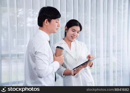 Manager advising guiding younger colleague with tablet in workplace. Couple businesspeople in formal wear working together on financial strategy as concept of teamwork and harmony in office.. Office colleague discussing business strategy for concept of harmony in office.