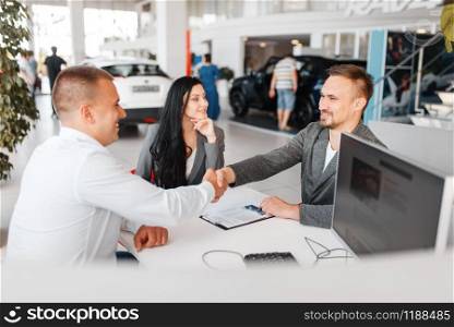 Manager and a couple make out the sale of a new car in the showroom. Male and female customers looks vehicle in dealership, automobile sale, auto purchase