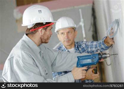 manager and young man using power drill on wall