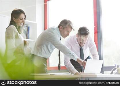 Manager explaining employees over laptop at desk in office
