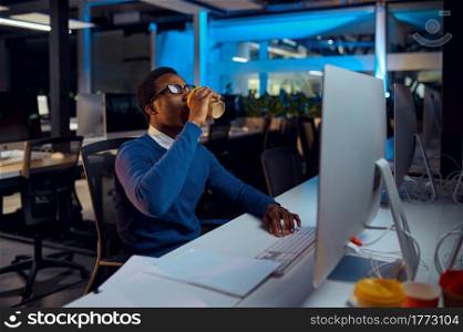 Manager holds cup of coffee, office lifestyle. Male person at laptop, dark interior on background, modern workplace. Manager holds cup of coffee, office lifestyle