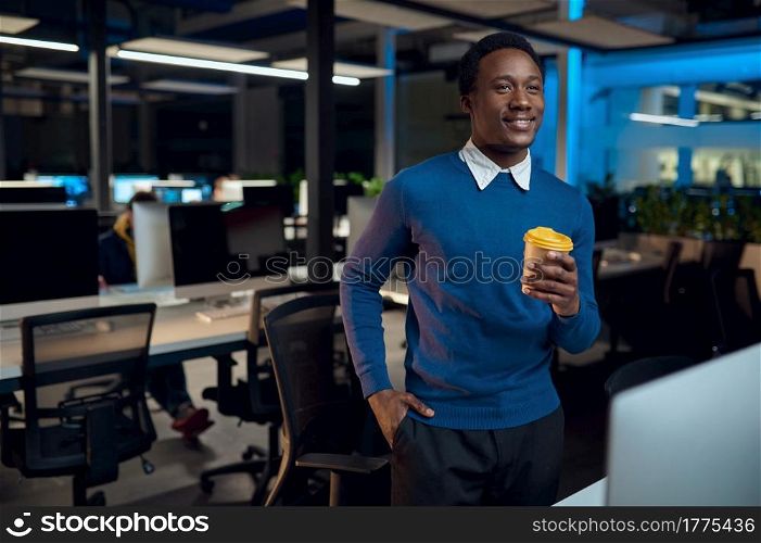 Manager holds cup of coffee, office lifestyle. Male person at laptop, dark interior on background, modern workplace. Manager holds cup of coffee, office lifestyle