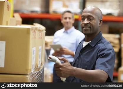 Manager In Warehouse With Worker Scanning Box In Foreground