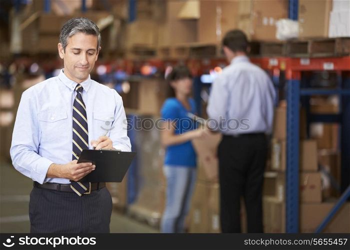 Manager In Warehouse Writing On Clipboard