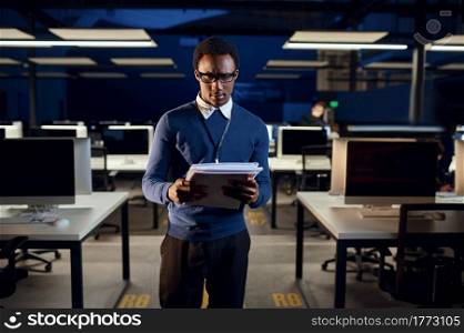 Manager looks in notebook, night office lifestyle. Male person the table, dark business center interior on background, modern workplace. Manager looks in notebook, night office lifestyle