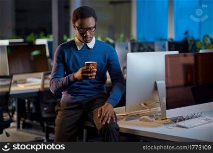 Manager poses with cup of coffee, office lifestyle. Male person at the table, dark business center interior on background, modern workplace. Manager poses with cup of coffee, office lifestyle