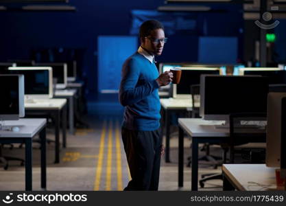 Manager poses with cup of coffee, office lifestyle. Male person at the table, dark business center interior on background, modern workplace. Manager poses with cup of coffee, office lifestyle