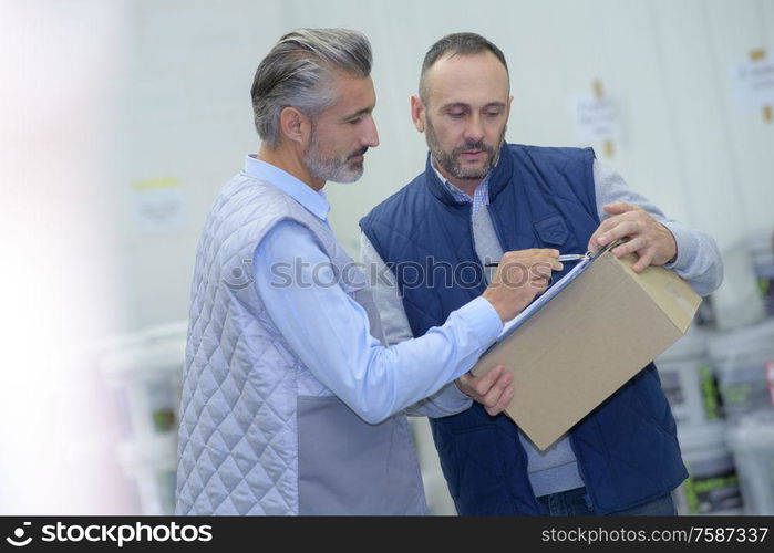 manager showing clipboard to worker in warehouse