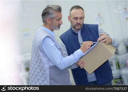 manager showing clipboard to worker in warehouse