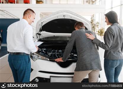 Manager shows the couple a new car in showroom. Male and female customers looks vehicle in dealership, automobile sale, auto purchase