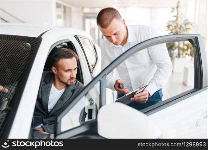 Manager shows to buyer price on new car in showroom. Male customer choosing vehicle in dealership, automobile sale, auto purchase