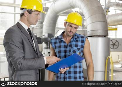 Manager with worker discussing over clipboard in industry