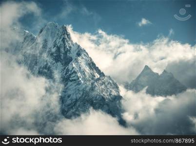Manaslu mountain with snowy peak in clouds in sunny bright day in Nepal. Landscape with high snow covered rocks and blue cloudy sky. Beautiful nature. Fairy scenery. Aerial view of Himalayan mountains