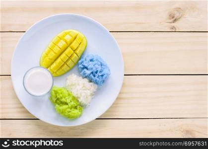 Mango and natural colored sticky rice with coconut milk, Thai de. Mango and natural colored sticky rice (colored blue with Pandanus leaf extract and colored blue with butterfly pea flower) with coconut milk on wooden table, Thai dessert