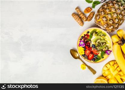 Mango banana pineapple turmeric breakfast superfoods smoothie bowl topped with fruits, berries and seeds. Overhead top view flat lay
