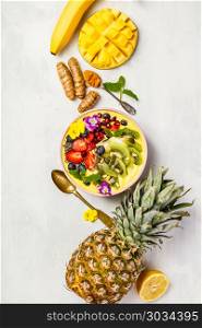 Mango banana pineapple turmeric breakfast superfoods smoothie bowl topped with fruits, berries and seeds. Overhead top view flat lay. Mango banana pineapple turmeric smoothie bowl