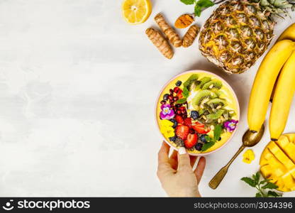 Mango banana pineapple turmeric breakfast superfoods smoothie bowl topped with fruits, berries and seeds. Overhead top view flat lay. Mango banana pineapple turmeric smoothie bowl