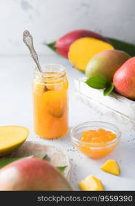 Mango marmalade jam puree with spoon on light background with raw fruits.