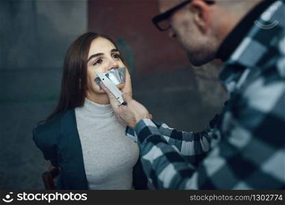 Maniac kidnapper taping his victim&rsquo;s mouth shut. Kidnapping is a serious crime, crazy male psycho, kidnap horror. Maniac kidnapper taping his victim&rsquo;s mouth shut