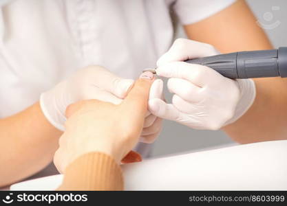 Manicure master applying electric nail file machine removing old nail polish on fingernails in a nail salon. Manicurist removing old nail polish