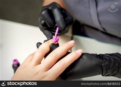 Manicure master applying pink nail polish to female nail in nail salon. Manicure master applying pink nail polish