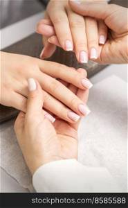 Manicure master holds hands of a young woman showing finished manicure on fingers in a nail salon. Manicurist showing manicure on fingers