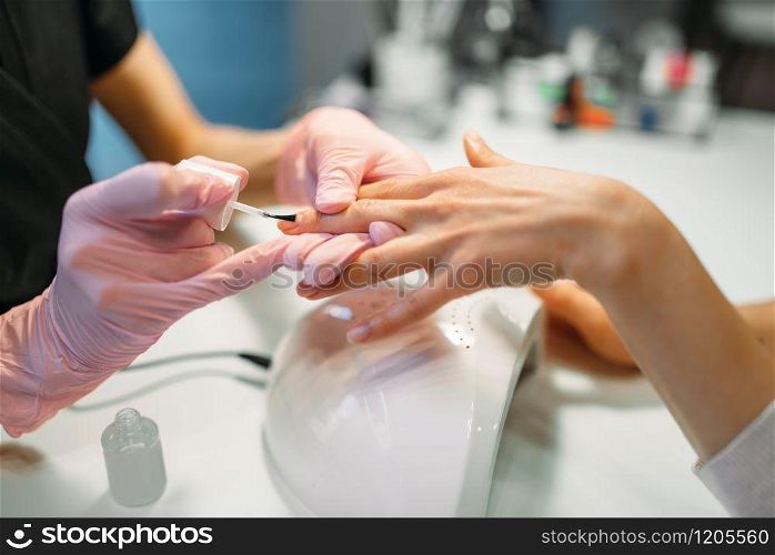 Manicure master in pink gloves applying nail varnish to female client, beauty salon. Manicurist doing fingernail care cosmetic procedure