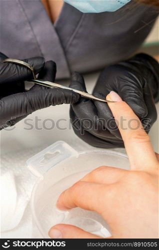 Manicure master removes cuticles from female nails with scissors wearing protective gloves in manicure salon. Manicure master removes cuticles from female nails with scissors wearing protective gloves in manicure salon.