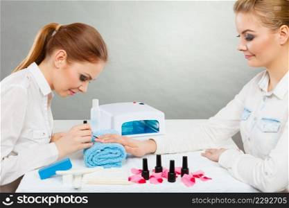 Manicure process concept. Young beautician and woman customer in beauty salon. Female client holds hands on deskop with nail polishes towel file lighting instruments.. Professional manicurist painting woman nails.