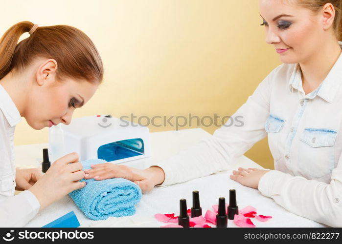 Manicure process concept. Young beautician and woman customer in beauty salon. Female client holds hands on deskop with nail polishes towel file lighting instruments.. Professional manicurist painting woman nails.