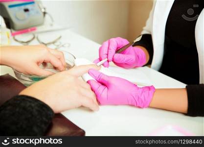 Manicure specialist in rubber gloves care by finger nail in spa beauty salon. Manicurist uses professional manicure tool. Manicure service.. Manicure specialist care by finger nail.