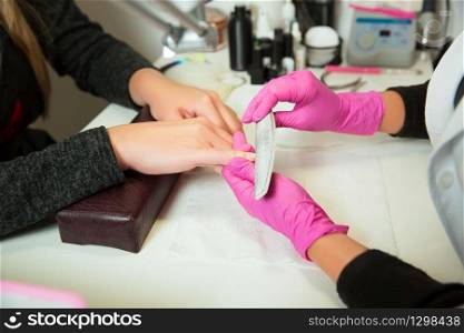 Manicure specialist in rubber gloves works with nailfile. Beauty salon.. Manicure specialist works with nailfile.