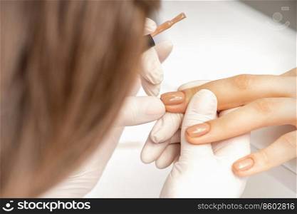 Manicurist applying beige nail polish on fingernails of a female client in a nail salon. Manicurist applying beige nail polish