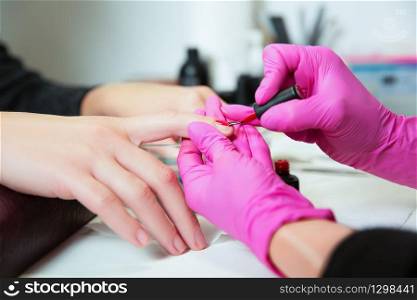 Manicurist in rubber gloves applies a lok on nails. Professional manicure tool.