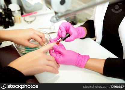 Manicurist in rubber gloves applies a lok on nails. Professional manicure tool.. Manicurist applies a lok on nails.