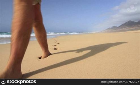 Mann geht am Strand entlang und hinterlS?t Fu?spuren im Sand.
