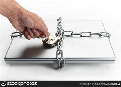 Mans hand placing key in padlock which is chained to closed laptop computer