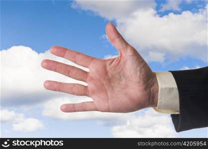 Mans hand, showing five fingers, cloudy blue sky background.