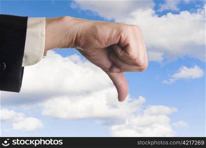 Mans hand, thumbs pointing down, cloudy sky background.