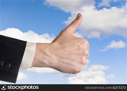 Mans hand, thumbs up, cloudy blue sky on background.