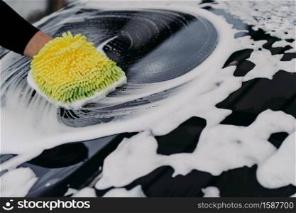 Mans hand washing black car with cloth and soap bubbles. Cleaning automobile. Selective focus. Carwsh concept.