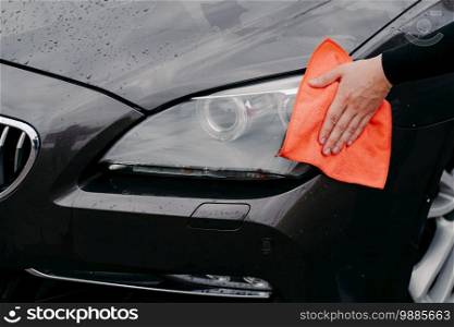 Mans hand wiping car headlight with microfiber cloth. Automobile detailing. Maintenance and transportation concept