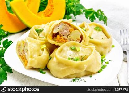 Manty steamed pies with minced meat and pumpkin, green onions in a plate, towel, parsley and fork on wooden board background