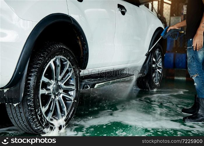 Manual Car Wash. Man using High Pressure Water Machine and Soap to Cleaning Car. Focus on Wheel