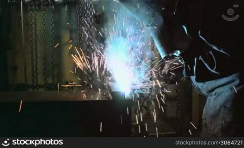 Manual job with worker in steel factory using welding mask, tools and machinery on metal