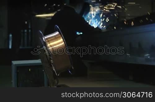Manual worker in steel factory using welding mask, tools and machinery on metal