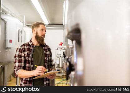 manufacture, business and people concept - man with clipboard working at craft brewery or beer plant. man with clipboard at craft brewery or beer plant